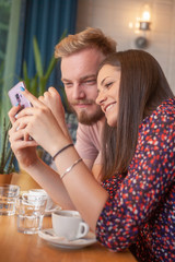 two friends sitting together, happy while looking at a phone screen together.