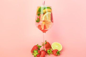 Glass of  fruit cocktail on pink background. Summer refreshing sweet water with strawberry, lime, mint leaves and lemon.
