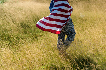 cropped view of soldier in camouflage uniform holding american flag in field