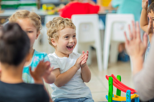 Happy children and pre-school teacher clapping hands in kindergarten