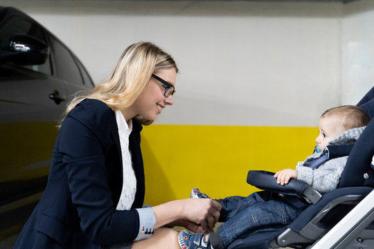 Young businesswoman with baby boy in stroller in a car park
