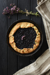 Homemade rustic pie. Blueberry galette in cast iron pan with linen cloth beside on dark background top view copy space