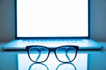 Computer eyeglasses in front of a laptop, low-key image. Blue light blockers and laptop in dark...
