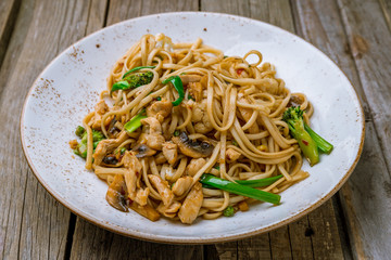 Udon noodles with chicken and vegetables on wooden background