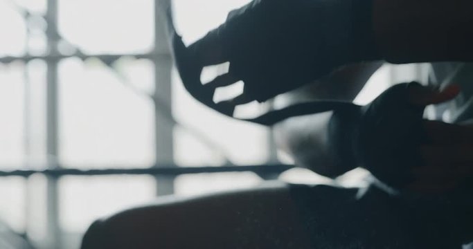 Cinematic slow motion close up shot of a professional young muscular african man is wrapping black bandages before to start practicing shadow boxing work out in a ring. 