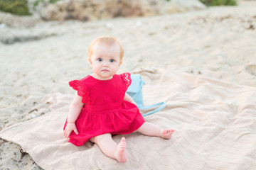 Little baby girl in red dress sitting on beach