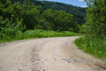 turn of a sandy stony road on a background of green trees and grass