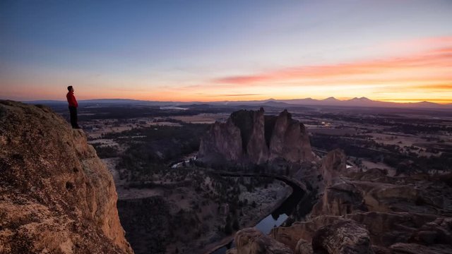 Man standing on top of a mountain is enjoying a beautiful landscape during a colorful and vibrant sunset. Taken at Smith Rock, Oregon, North America. Still Image Continuous Animation