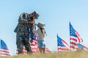 selective focus of kid touching uniform of military father near american flags