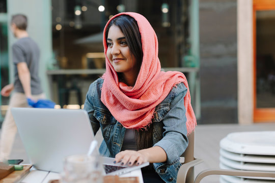 Smiling young woman with laptop wearing headscarf at a pavement cafe