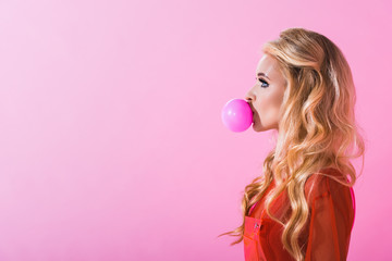 side view of beautiful girl blowing bubble gum on pink, doll concept