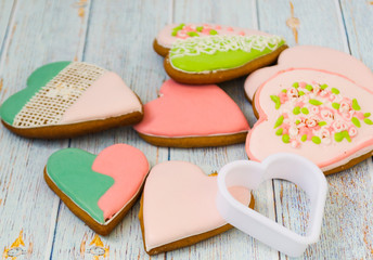 Pink and colored gingerbread and honey cakes and heart-shaped cookies lie in a messy pile on a light wooden background. Nearby are white molds for baking. Place for text. The concept of love, mother's