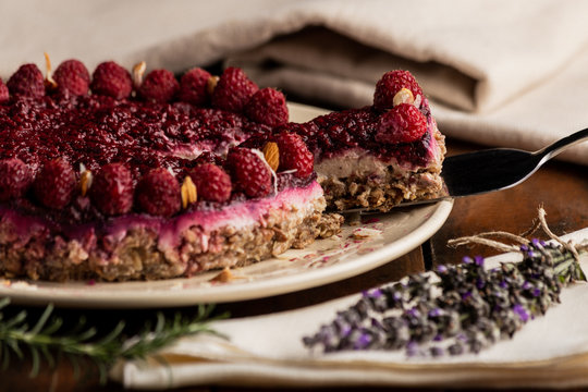 Sliced juicy fruit cake with raspberries on white plate on wooden background decorated with lavender bouquet