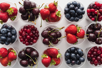 Fototapeta na wymiar top view of whole cranberries, fresh strawberries, blueberries and cherries in plastic cups