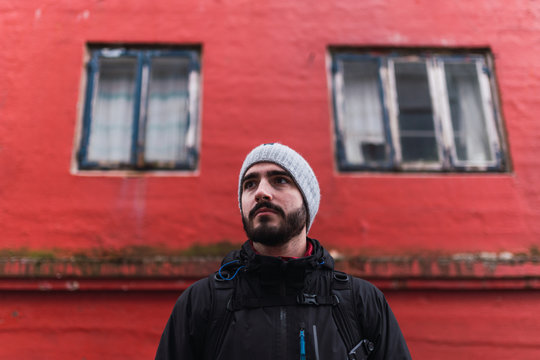 bearded man looking away while standing in front of red building in faroe island