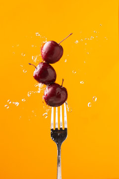 Composition of tasty juicy cherries on a fork with splashing water on bright yellow background