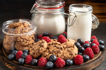 Biscuits, milk, flour recipients and forest fruits placed on rounded wooden platter close-up.