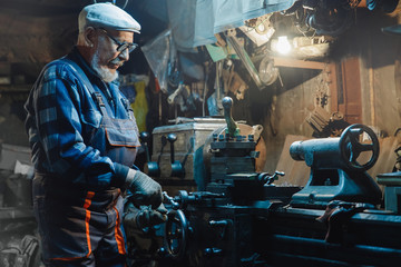 Senior elderly male turner mechanic working on machine tool for metal