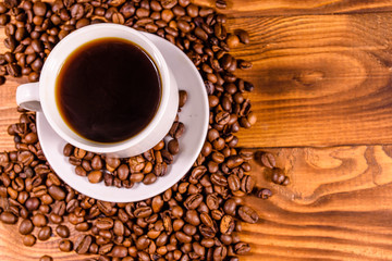 Cup of hot coffee and scattered coffee beans on wooden table. Top view