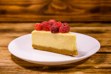 White plate with cheesecake New York and raspberries on wooden table