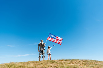 Back view of kid in straw hat and military father holding American flags - obrazy, fototapety, plakaty