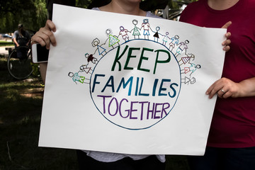 Two women at protest holding homemade sign together that says keep families together with world and...