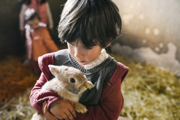 Cute little boy holding lovely little bunny standing in sunlight in nature
