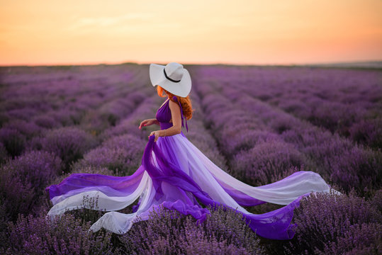 Young woman in luxurious purple dress standing in lavender field, rear view