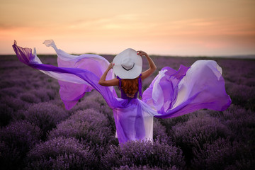 Young woman in luxurious purple dress standing in lavender field, rear view