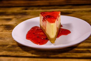 White plate with cheesecake New York and raspberry jam on wooden table