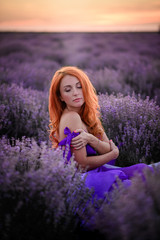 Gentle portrait of young red-haired woman who sits in lavender field at sunset