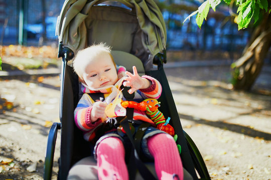 girl in bright stylish clothes sitting in pushchair outdoors on a fall day