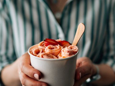 Rolled ice cream with strawberry in cone cup in woman hands. Hand holding cone cup with thai style rolled ice cream