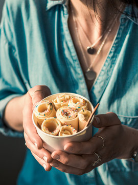 Rolled ice cream in cone cup in woman hands. Woman in jeans shirt holds cone cup with thai style vanilla rolled ice cream. Vertical