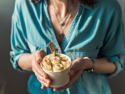 Rolled ice cream in cone cup in woman hands. Woman in jeans shirt holds cone cup with thai style vanilla rolled ice cream