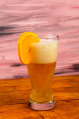 Orange Slice on Glass of Wheat Beer with Frothy Head on Rustic Picnic Table
