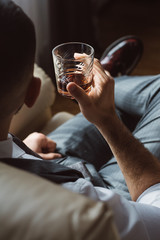 Rear view of young man holds glass of brandy. Tasting and degustation concept. Businessman in elegant suit with glass of whiskey. Sommelier tastes expensive drink.