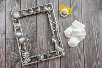 Baby accessories for newborns: baby photo frame, socks and soother on wooden background. Motherhood concept. Top view, flat lay composition. Copy space for text.