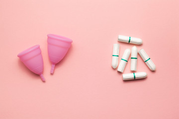 Two reusable silicone menstrual cups and tampons comparison on a soft pink background. Modern female intimate alternative gynecological hygiene. Eco zero waste concept