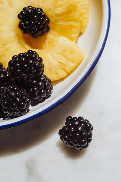 From above yellow juicy slices of pineapple and ripe blackberry served on white background