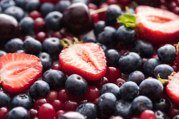 selective focus of red, fresh and ripe cranberries, cut strawberries, blueberries and cherries