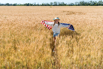 cute and happy child holding american flag with stars and stripes in golden field