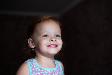 beautiful happy cute little redhead girl smiles sincerely and laughs with a soft light from the window lifestyle