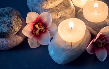 Spa with burning white candles standing on stones and flowers