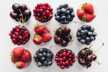 top view of whole cranberries, strawberries, blueberries and cherries in plastic cups