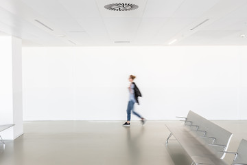Motion blur of woman walking at contemporary white empty hallway.