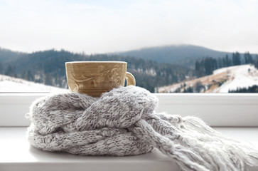 Hot drink and warm scarf near window with view of winter mountain landscape