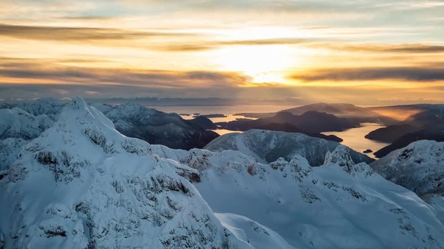 Beautiful aerial landscape view of the snow covered mountains surrounded with clouds during  a colorful sunset. Picture taken from an airplane near Squamish, North of Vancouver, BC, Canada. 