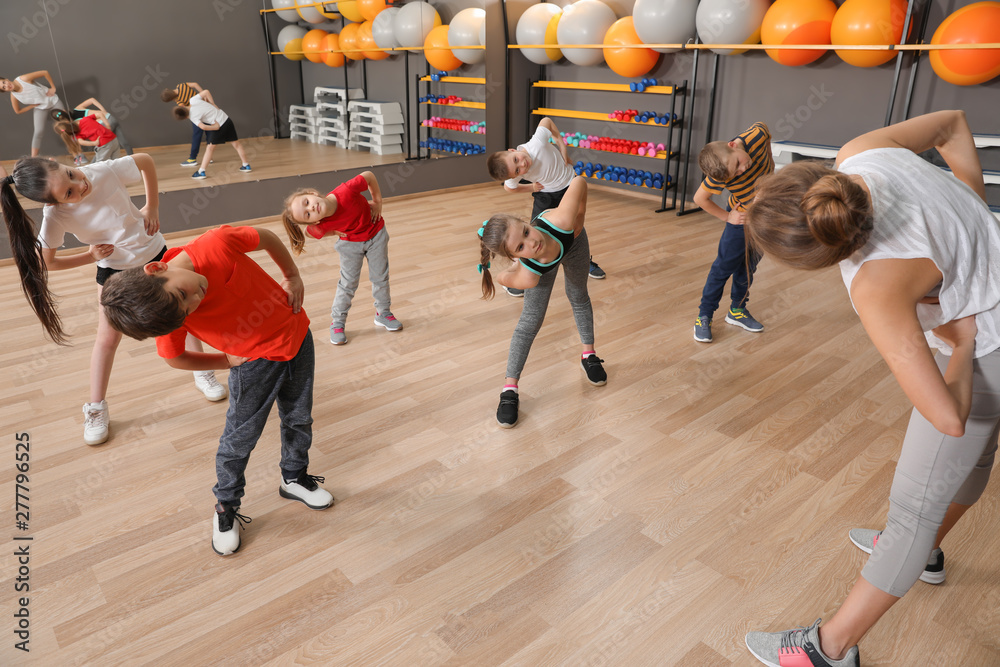 Wall mural cute little children and trainer doing physical exercise in school gym. healthy lifestyle