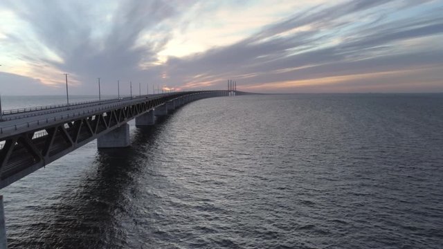 Aerial view of Øresund Bridge at dusk. Drone shot flying over sea and bridge, driving cars at sunset. Connection between Malmö, Sweden and Copenhagen, Denmark